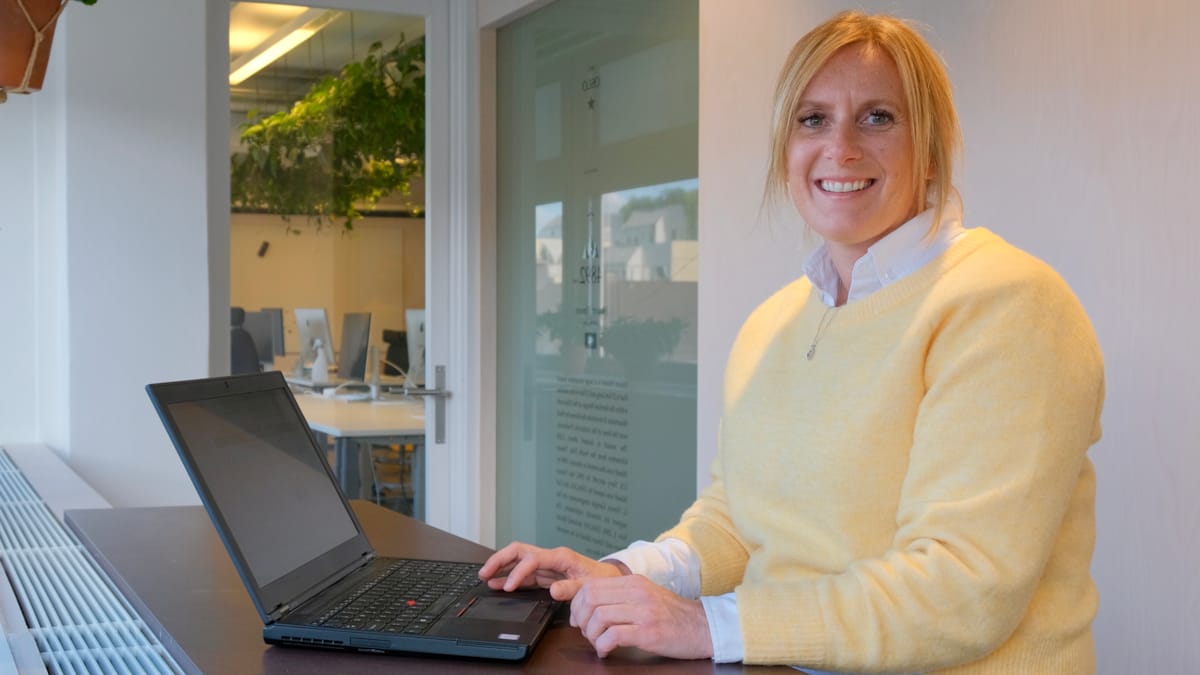 Aud Marie sitter med en laptop på bordet foran seg. På seg har hun en gul genser.
