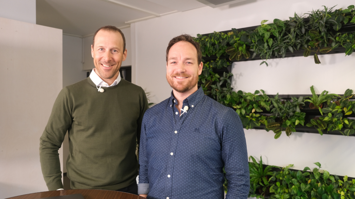 Fredrik og Arild står ved et bord, i bakgrunnen ser vi Epinova-logoen på veggen