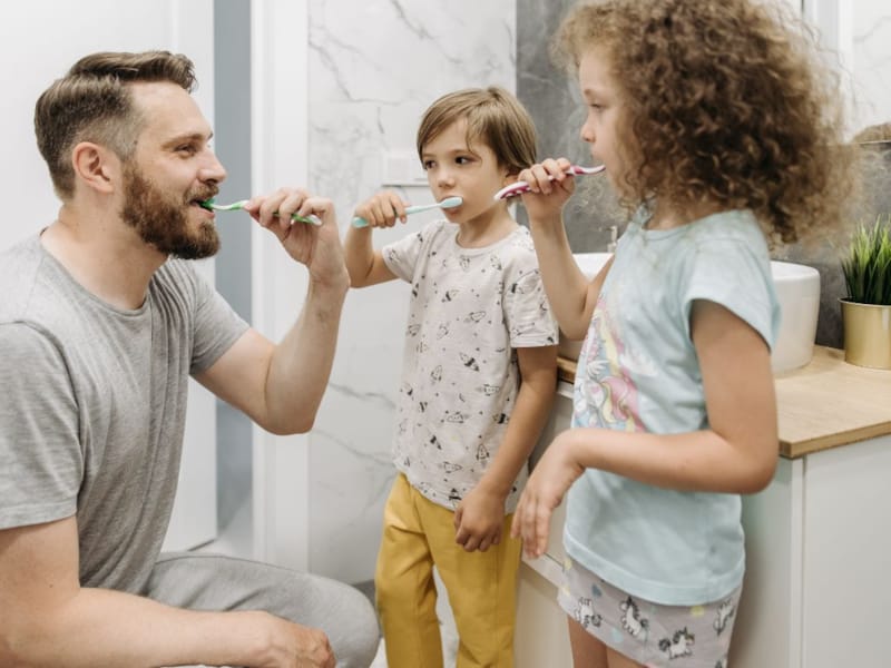 Bilde av en mann som pusser tennene sine sammen med to barn.